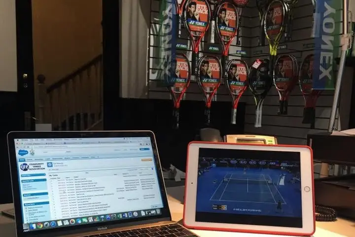 Laptop and iPad in front of a wall of Yonex rackets